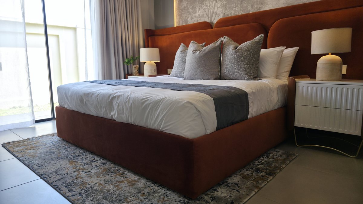 Guest bedroom with a rust-coloured upholstered bed, layered pillows and bedside lamps.