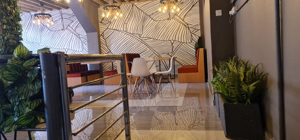 Restaurant interior with patterned wall panels, pendant lights, dining chairs and indoor planting.