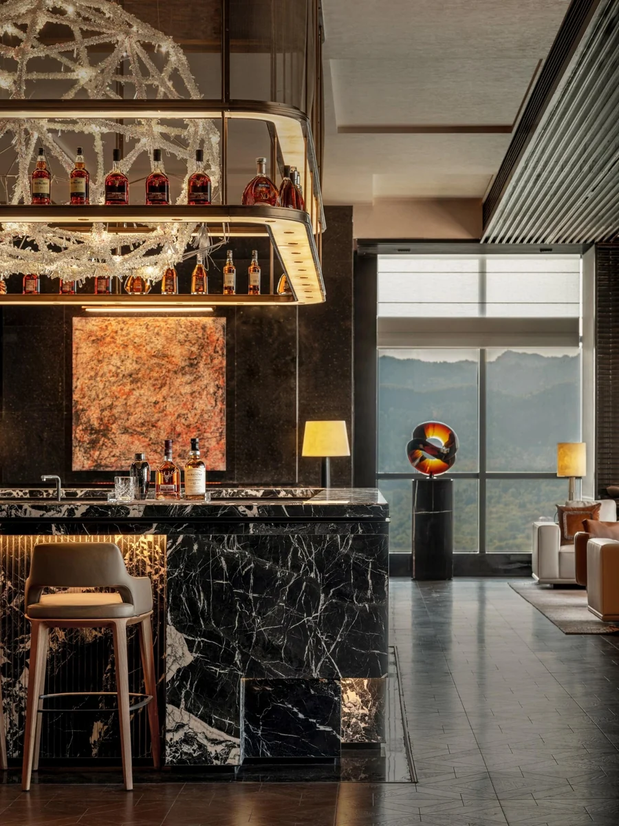 Bar interior with a dark veined counter, illuminated shelving, decorative lighting and upholstered seating.
