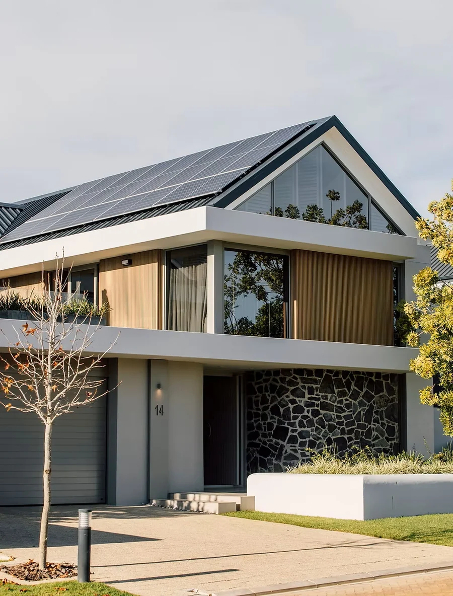 Modern house exterior with a pitched roof, solar panels, large glazing and timber-toned cladding.