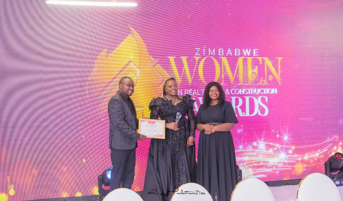 Three people holding a certificate and trophy against the pink Zimbabwe Women in Real Estate & Construction Awards backdrop.